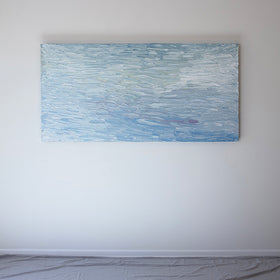 A abstract painting with blue textured brushstrokes is hung on the wall in the artists studio.