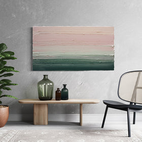 A light Coral, light pink, celadon and hunter green thickly textured abstract painting by Teodora Guererra hanging on a wall over a low natural wood table with green bottles on it. To the right is a contemporary black chair and to the left is a potted tree.