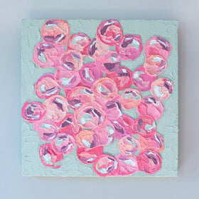 A very textured painting with celadon background and circle type abstract flowers in pink, peach, plum and white hangs on a white wall.