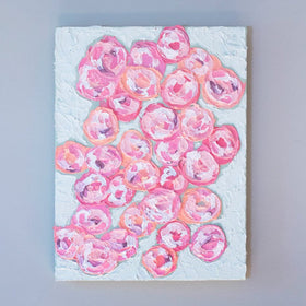 A very textured abstract painting with celadon background and circle type abstract flowers in pink, peach, plum and white hangs on a grey wall.