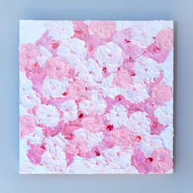 A close up of a very textured abstract painting with white background and circle type abstract flowers in pink and white hangs on a grey wall.
