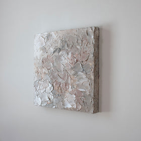 A painting is shown hanging on the wall at an angle. Its surface is decorated with white, pink and grey paint in a thick impasto. Wired and ready to hang.