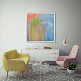 A blue, orange and green abstract print in a white floater frame hangs on a white wall above a white console cabinet, a yellow sofa, a pink rocking chair and a small white wire coffee table with a stack of books.
