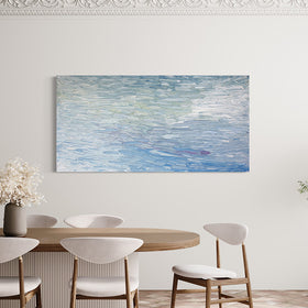 A abstract painting with blue textured brushstrokes is seen hanging on a wall in a dining room over a table with white contemporary chairs and a potted tree to the right.