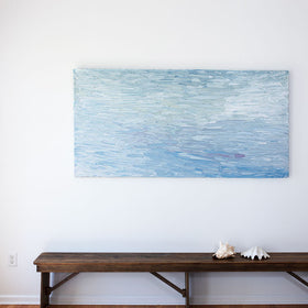 A abstract painting with blue textured brushstrokes is hung above a bench with sea shells on it.