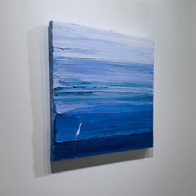 A blue and white textured abstract painting by Teodora Guererra hangs on a white wall, side view.