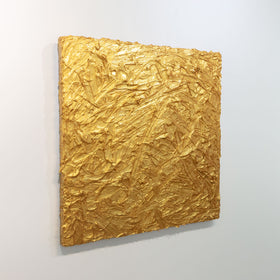 A metallic gold thick textured painting by Teodora Guererra is seen at an angle on a gallery wall.