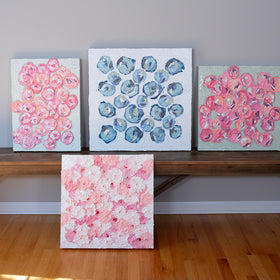 A group of very textured abstract paintings sit and lean on a bench in the artists studio.