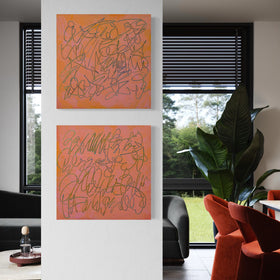 Two abstract text based paintings in orange and pink tones hanging vertically on a white wall in a modern living room setting.