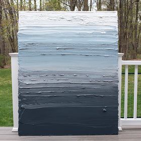 A dark grey blue, light blue, blue green, and white thickly textured abstract painting leaning on a deck outside in natural light by Teodora Guererra.