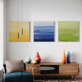 Three textured abstract paintings, one in yellow and white, another in blue and white and the last in chartreuse and white by Teodora Guererra hang on a wall over a credenza with bright colored ceramic pots.