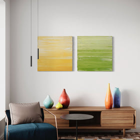 Two textured abstract paintings, one in yellow and white and the other in chartreuse and white by Teodora Guererra hang on a wall over a credenza with bright colored ceramic pots.
