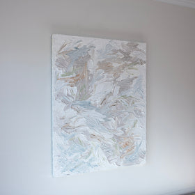 An abstract painting with thickly textured brushstrokes of beige, green, orange, and blue is seen at an angle on a gallery wall.