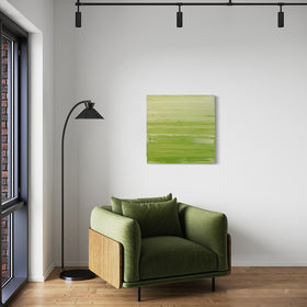 A chartreuse green and white textured abstract painting by Teodora Guererra hangs on a wall over a fabric green chair with a black modern floor lamp to the left.