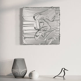 A silver metallic textured painting by Teodora Guererra hanging on a wall above a white shelf with decorative objects.