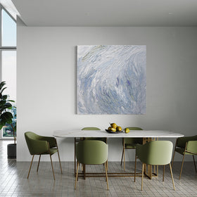 A Grey blue, light blue, lavender, celadon and white thickly textured abstract painting by Teodora Guererra hanging on a white wall in a dining room over a white marble table with gold brass legs and modern green chairs with a plate of green pears sitting on the table. To the left is a glimpse of the living room.