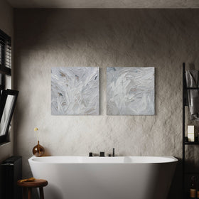 A pair of thickly textured paintings in grey, white, blue grey and plum grey by Teodora Guererra hanging on a wall in front of a modern bath tub.