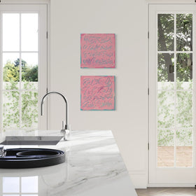 Two square pink abstract art prints with blue calligraphic patterns hang on a white wall in a bright kitchen with white French doors and a marble countertop.