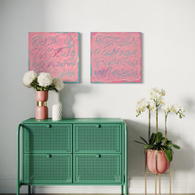 A styled interior scene showing two pink abstract wall art prints hanging above a mint green cabinet, with flowers and a potted orchid in a room with a white wall and light wood floor.