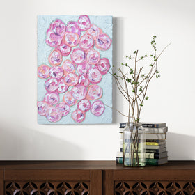 A very textured abstract painting with celadon background and circle type abstract flowers in pink, peach, plum and white hangs on a white wall above a credenza with books and a glass vase holding branches with green buds.