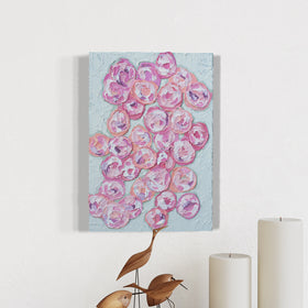 A very textured abstract painting with celadon background and circle type abstract flowers in pink, peach, plum and white hangs on a white wall above a marble counter with 2 white candles and wooden bird sculptures.