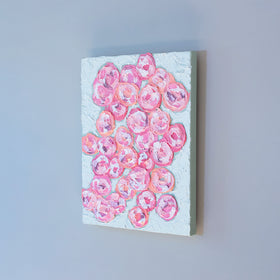 A very textured abstract painting with celadon background and circle type abstract flowers in pink, peach, plum and white hangs on a grey wall.