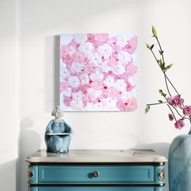 A very textured abstract painting with circle type abstract flowers in pink and white hangs on a white wall above a teal end table with a white marble top.