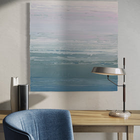 A teal blue, teal green, lavender and pale lavender textured abstract painting by Teodora Guererra hangs on a white wall. above a maple table with a lamp and 2 decorative vases. A blue chair sits in front.