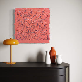A square abstract painting with textured coral-pink background and dark scribbled line work, displayed on a light gray wall above a dark wooden console table with a yellow lamp and ceramic vases.