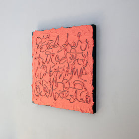 A square abstract painting with a textured coral-pink surface and dark calligraphic line work, mounted against a light gray wall.