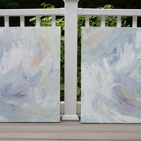 A pair of thickly painted paintings in teal, sea foam green, celadon, white, lavender and yellow by Teodora Guererra lean on a deck in the sunlight outside.