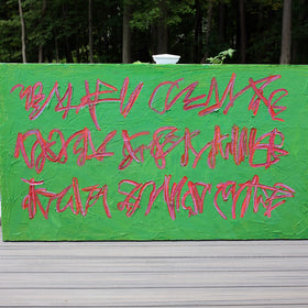 An original green canvas painting with red graffiti-style lettering, displayed on a gray wooden deck railing with a forest background.