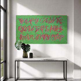 An original abstract green painting featuring red graffiti-style lettering, displayed in a modern interior setting above a white console table with a black metal frame and a green monstera plant.