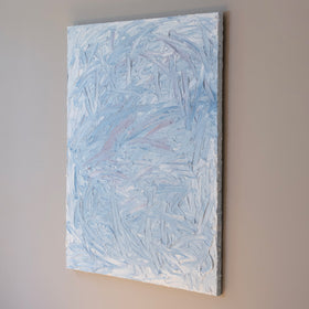 A blue and white textured painting hangs from a side view on a grey wall in the artists studio.