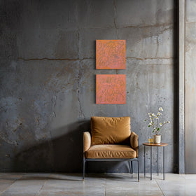 Two square orange abstract text based paintings with carved teal scribbled lines hang on a textured gray concrete wall above a mustard yellow armchair and a small side table with flowers.