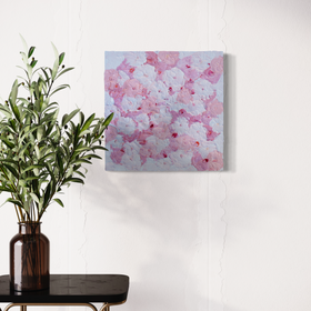 A close up of a very textured abstract painting with circle type abstract flowers in pink and white hangs on a white wall above an end table with a glass vase holding eucalyptus branches.