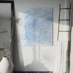 A blue and white textured painting hangs on a white wall above a blue tiled floor. A decorative ladder leans to the right and ceramic pot with branches and mirror are to the left.