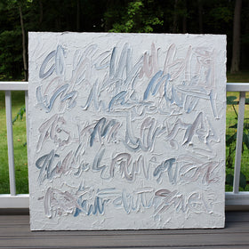 A square canvas painting with thick, textured impasto brushstrokes in shades of gray, blue, and beige, leaning against a white wooden railing on a deck with a green forest background.