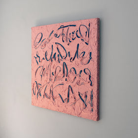 A coral/pink text based painting featuring navy abstract calligraphic lettering, displayed against a neutral light gray wall, side view.