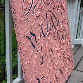 An abstract textured canvas painting leaning against a white railing on a wooden deck. The artwork features a thick, impasto pink background with dark navy blue calligraphic brushstrokes.
