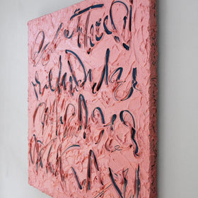A square pink canvas painting with thick, textured impasto brushstrokes and navy calligraphic lettering, shown hanging on a light gray wall.