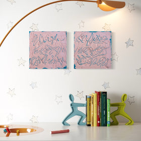 A styled interior scene with two pink abstract texted based paintings hanging on a white wall, a curved brass floor lamp, decorative star decals, a white table, books, and two colorful figurine bookends.
