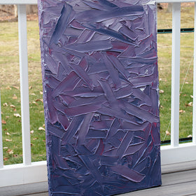 A tonal purple and pink thickly textured abstract painting by Teodora Guererra leans on a deck outside in the natural light.