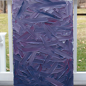 A tonal purple and pink thickly textured abstract painting by Teodora Guererra sits on a deck outside in the natural light.