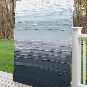 A dark grey blue, light blue, blue green, and white thickly textured abstract painting leaning on a deck outside in natural light by Teodora Guererra.