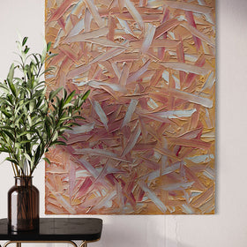 A orange, pink, coral and white thickly textured abstract painting hangs on a white wall. Sitting in front is a black marble table with brass legs. On the table sits an amber glass vase with eucalyptus branches.