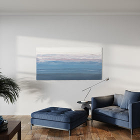 A blue, light pink, coral and white thickly textured abstract painting by Teodora Guererra on a white wall in natural light hangs over a blue oversized chair with ottoman. A contemporary end table is to the side of the chair with a modern light. Also, two plants are on either side and a coffee table is to the left with one blue bottle and other on it.