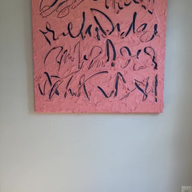 A video of a coral/pink text based painting featuring navy abstract calligraphic lettering, displayed against a neutral light gray wall.