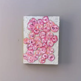 A video of a very textured abstract painting with celadon background and circle type abstract flowers in pink, peach, plum and white hanging on a grey wall.