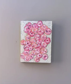 A video of a very textured abstract painting with celadon background and circle type abstract flowers in pink, peach, plum and white hanging on a grey wall.